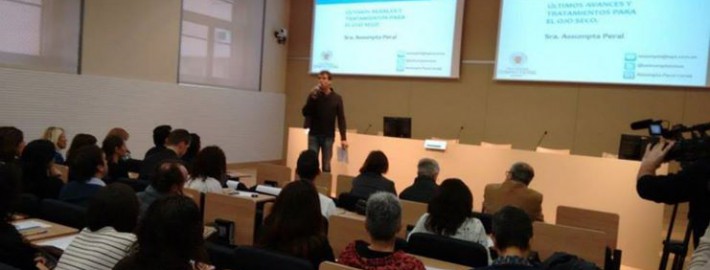 Un home està dret parlant per un micròfon davant d'un públic en una sala de conferències. Les diapositives de la presentació sobre els avenços en el tractament de l'ull sec es projecten en pantalles darrere seu. Diverses persones escolten atentament.