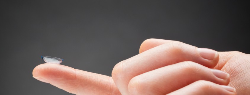 Primer pla d'una mà que sosté una lent transparent Orto-K a la punta del dit índex sobre un fons llis i fosc.