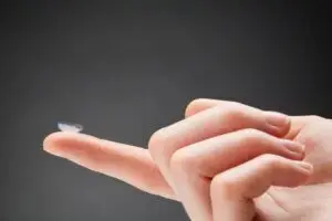 Primer pla d'una mà que sosté una lent transparent Orto-K a la punta del dit índex sobre un fons llis i fosc.