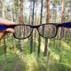 Una mà sosté unes ulleres davant d'un bosc, fent que els arbres apareguin nítids i clars a través de les lents mentre que la zona circumdant roman borrosa, il·lustrant vívidament els efectes de la miopia.